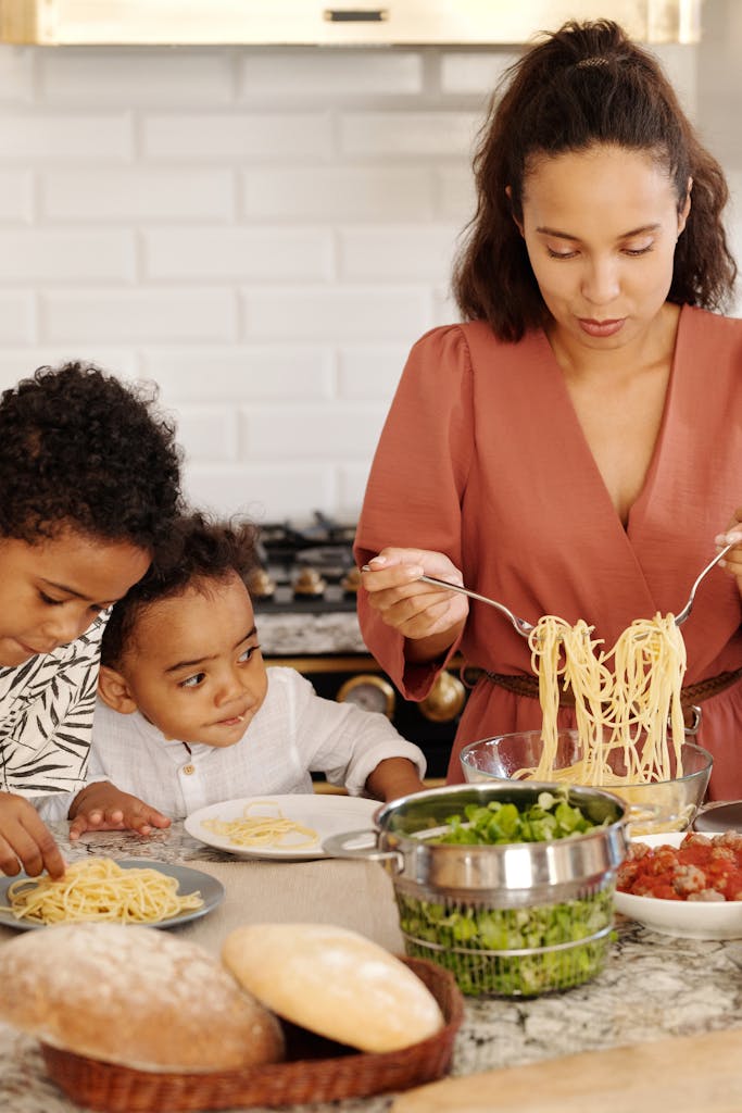 A mother prepares pasta with her children in a modern kitchen, creating a warm family moment indoors.