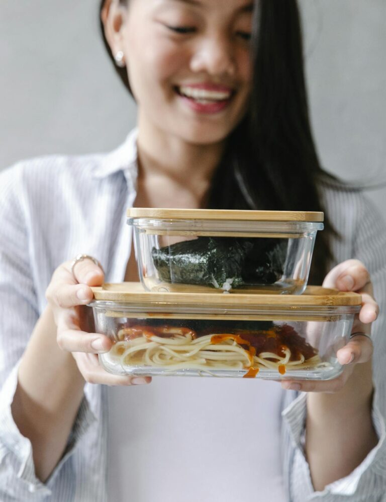 Smiling Asian woman holding two bento boxes filled with delicious food indoors.