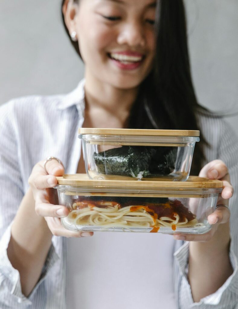 Smiling Asian woman holding two bento boxes filled with delicious food indoors.