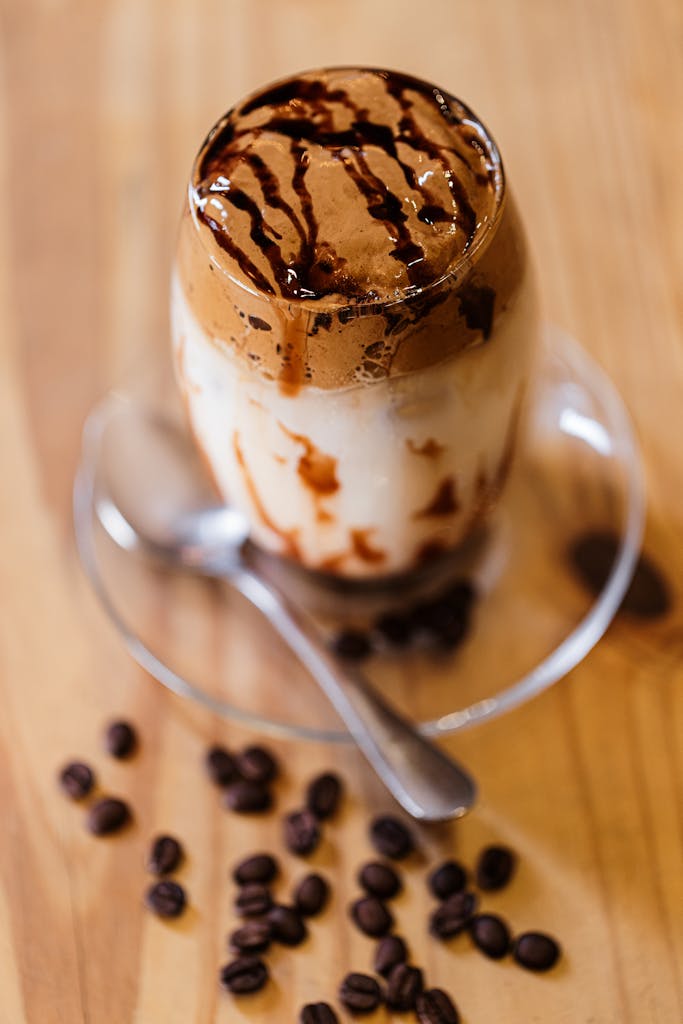 A delicious iced coffee topped with chocolate sauce drizzled over the frothy layer, with scattered coffee beans.