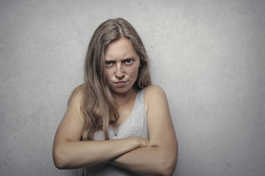 A woman with arms crossed showing a fierce expression against a gray background.