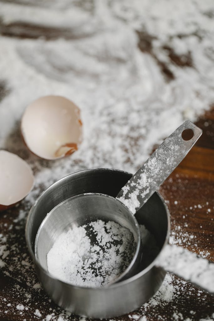 Close-up of flour, eggshells, and baking utensils on a wooden surface, perfect for food blogs.