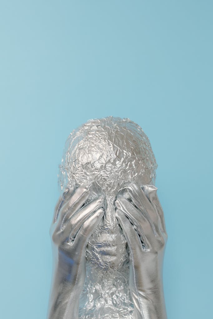 Conceptual silver alien with gloves against blue background, studio shot.