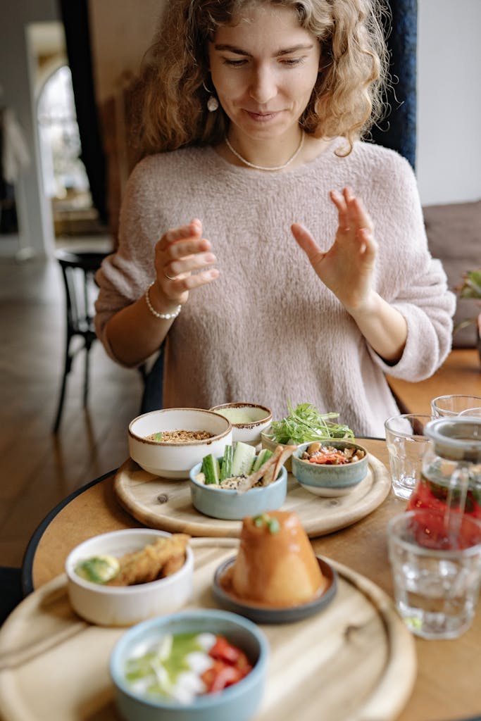 A woman in a sweater enjoying a variety of small dishes at a dining table indoors.