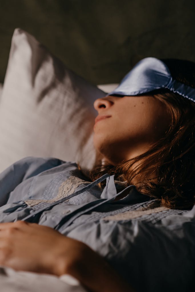 A woman resting peacefully in bed with a blue eye mask covering her eyes, capturing a serene bedtime moment.