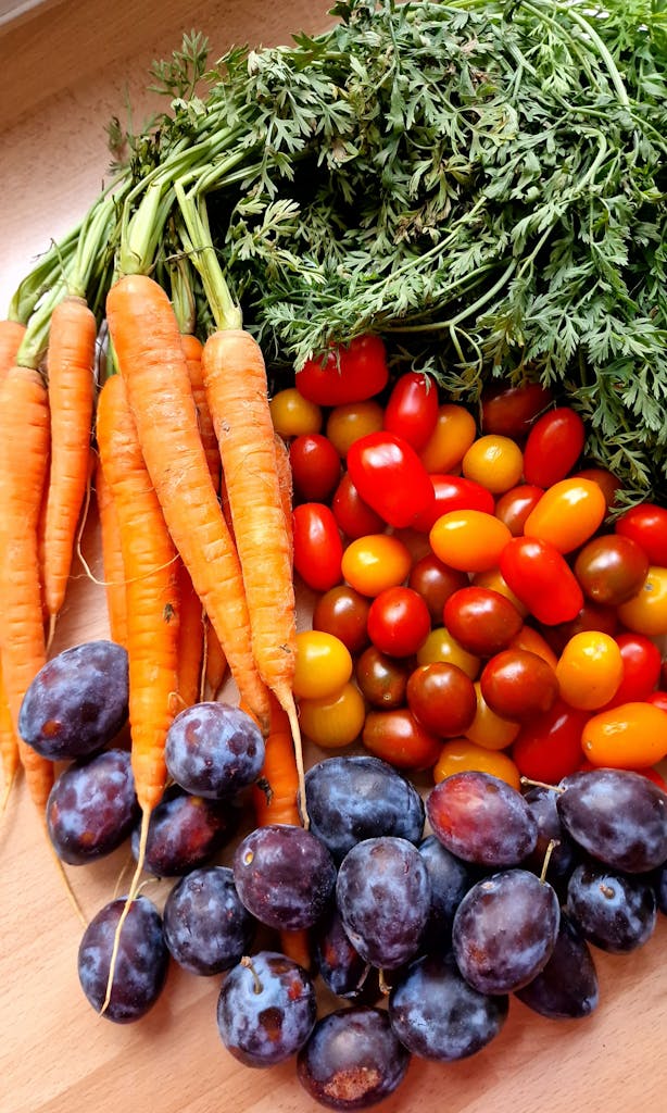 An artistic arrangement of fresh carrots, cherry tomatoes, and plums. Perfect for healthy meals.