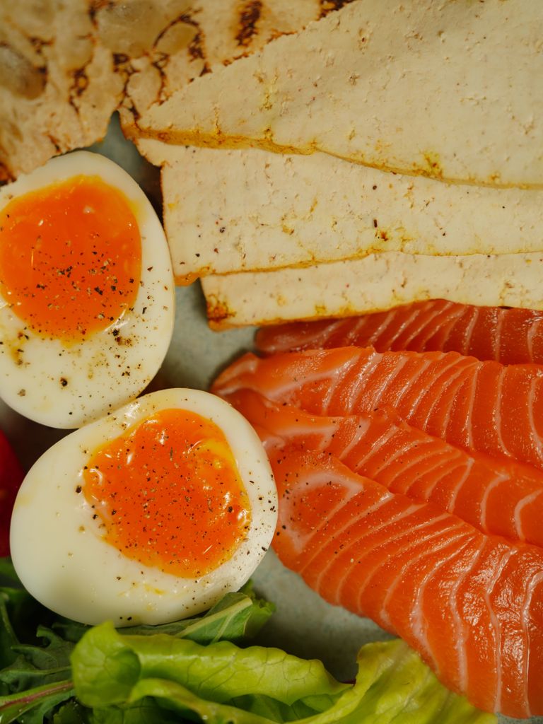 A delicious vertical shot of sliced salmon, boiled eggs, tofu, and greens, perfect for lunch or dinner.