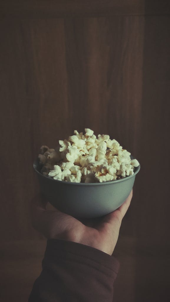 A person holds a bowl of popcorn, creating a cozy, cinematic atmosphere.
