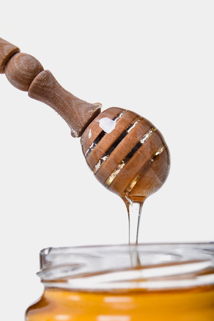 Sweet golden honey flowing from a wooden dipper, highlighting its thick, sticky texture.