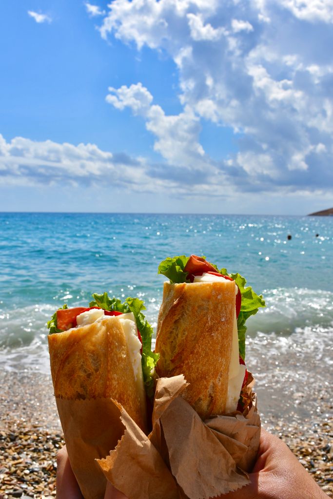 Baguette sandwiches held at a beach with clear blue skies and ocean waves.