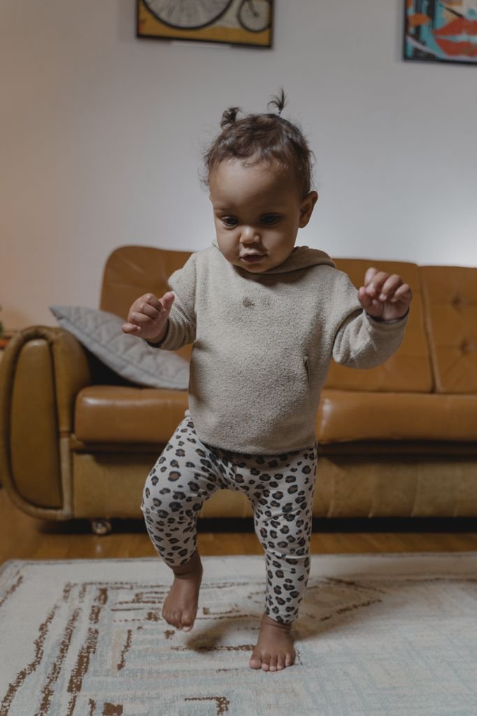 Cute baby taking first steps in a cozy, carpeted living room setting.