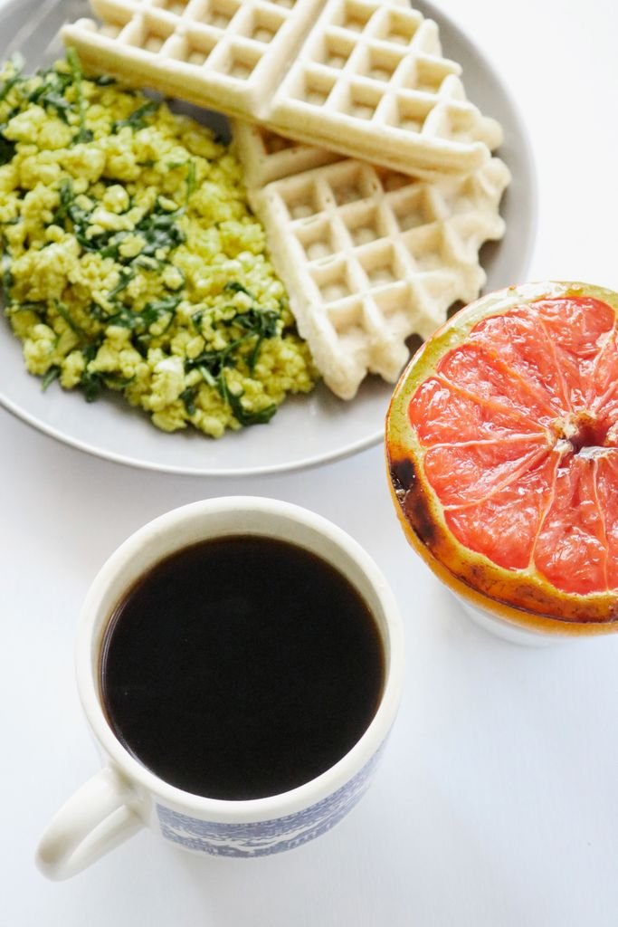 Tasty breakfast featuring coffee, scrambled eggs, waffles, and grapefruit.