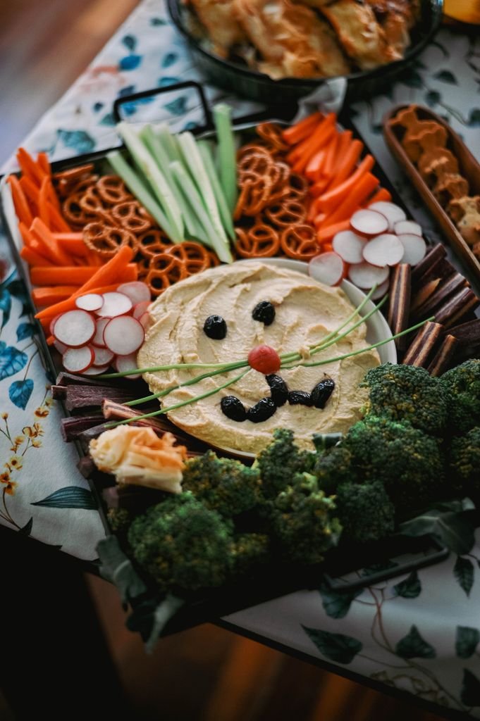 A colorful vegetable snack tray arranged to resemble an animal face with hummus and veggies.